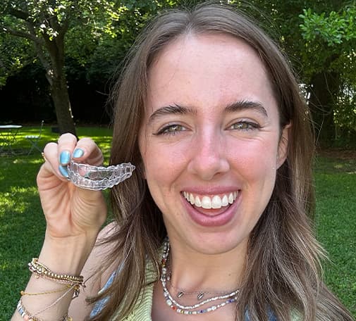 Real Smile Express patient Brynne F. smiling holding aligners up